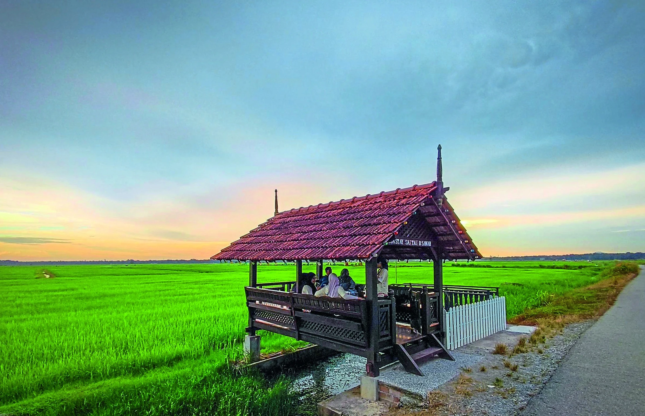 A small shelter beside green paddy fields in Muar at sunset