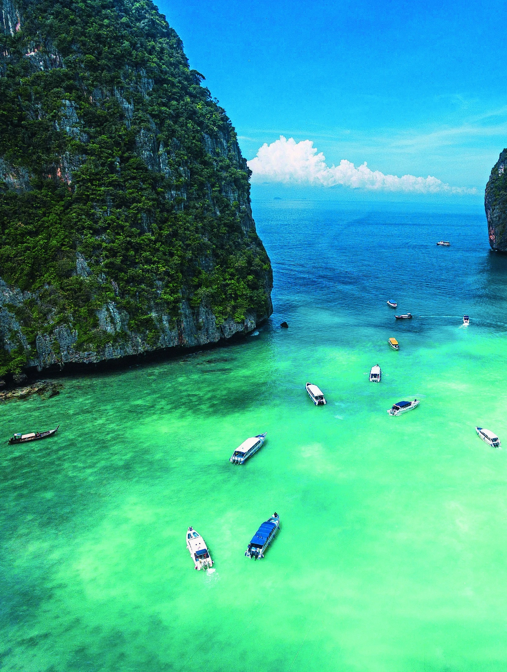 Small boats float in turquoise water beneath Krabi’s towering limestone cliffs