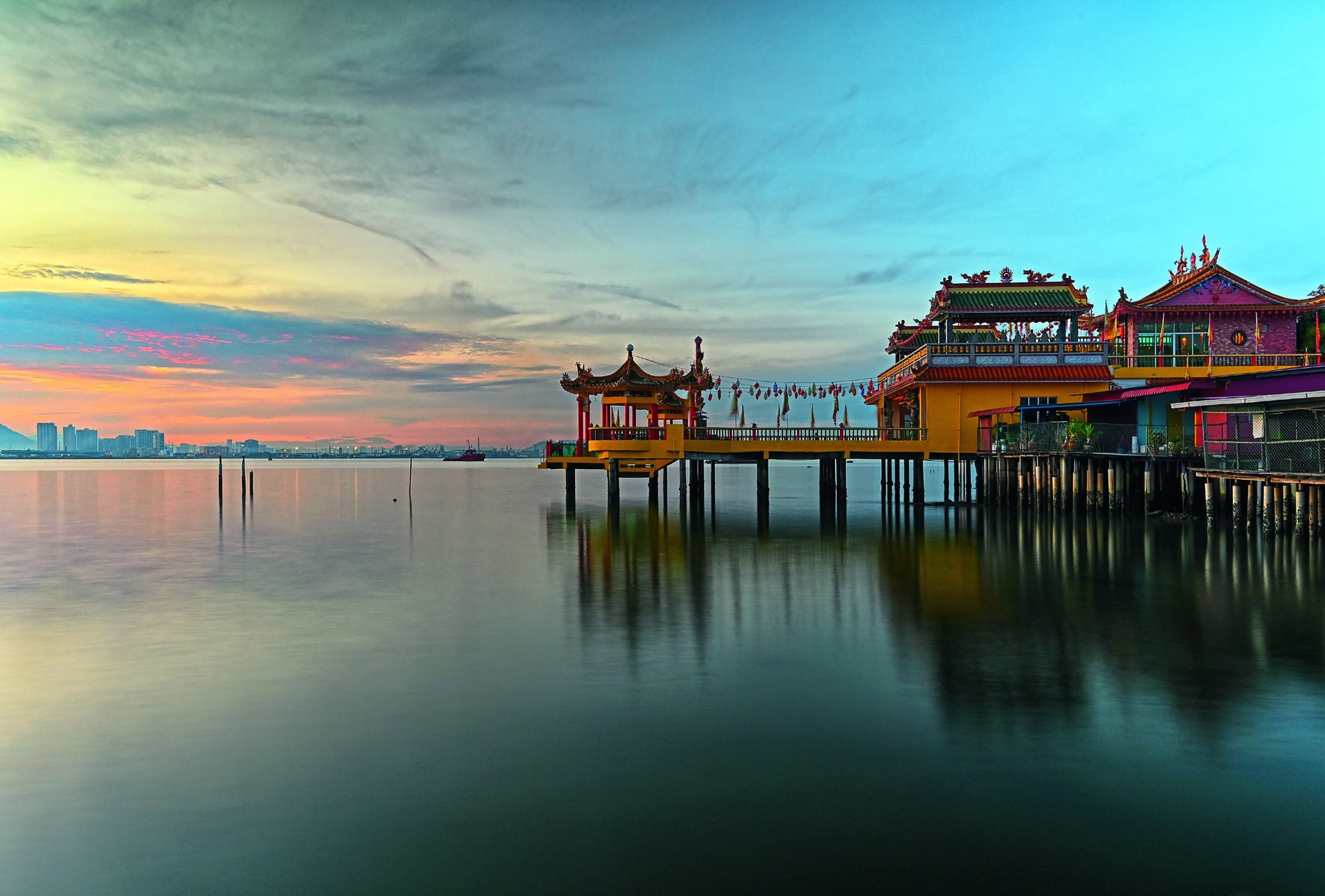 A waterfront temple reflected in the calm sea in Penang at sunset