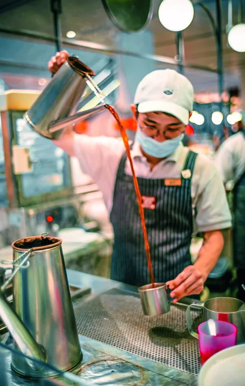 A tea maker pulls a long stream of teh tarik between two metal containers